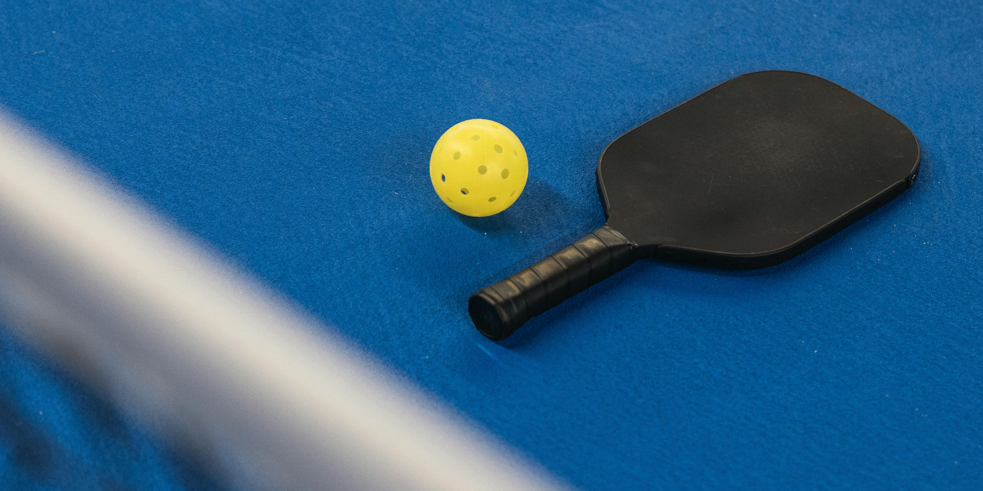 A pickleball paddle and ball on a blue court