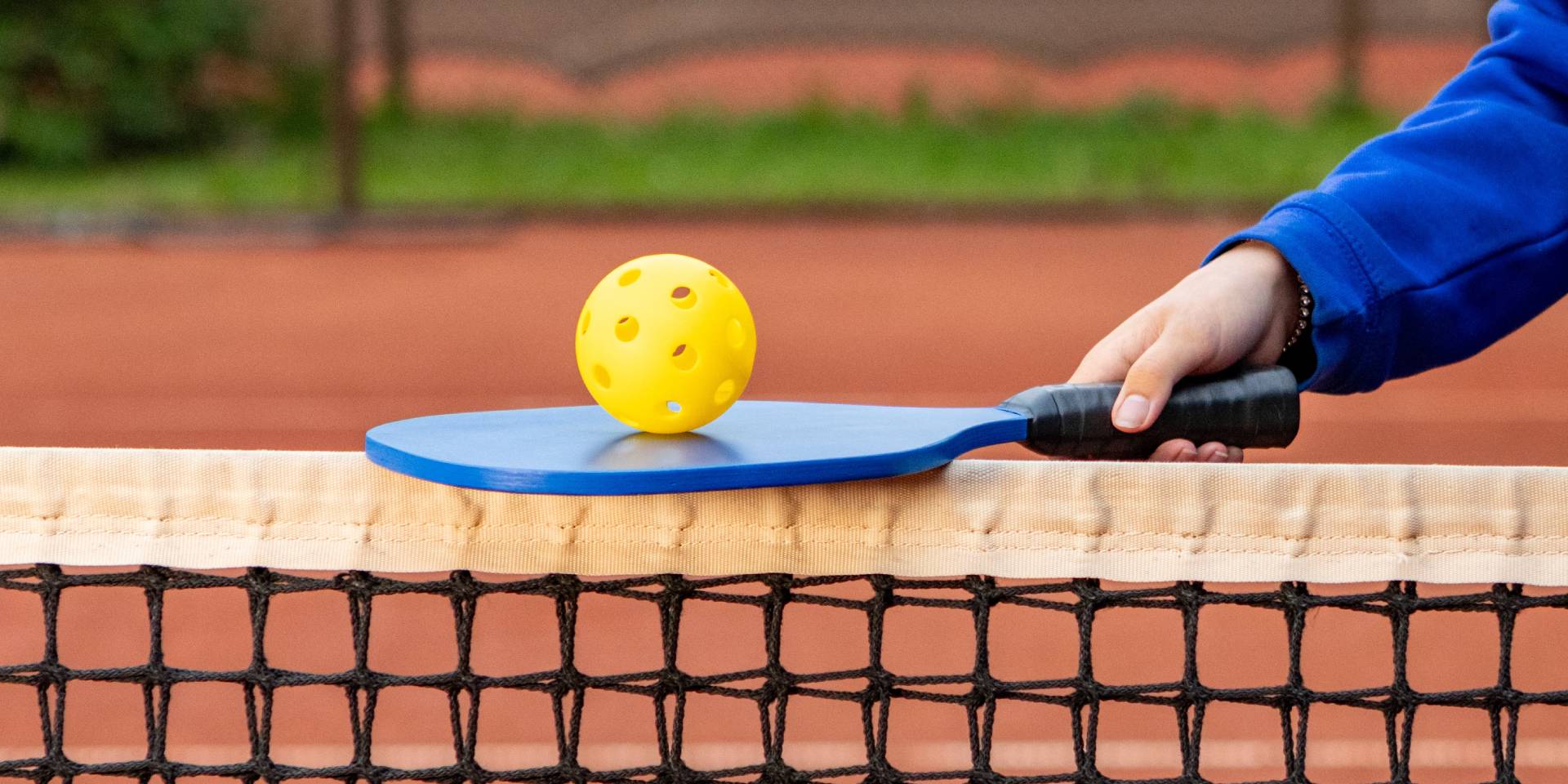 Someone balancing a pickleball paddle on a pickleball net