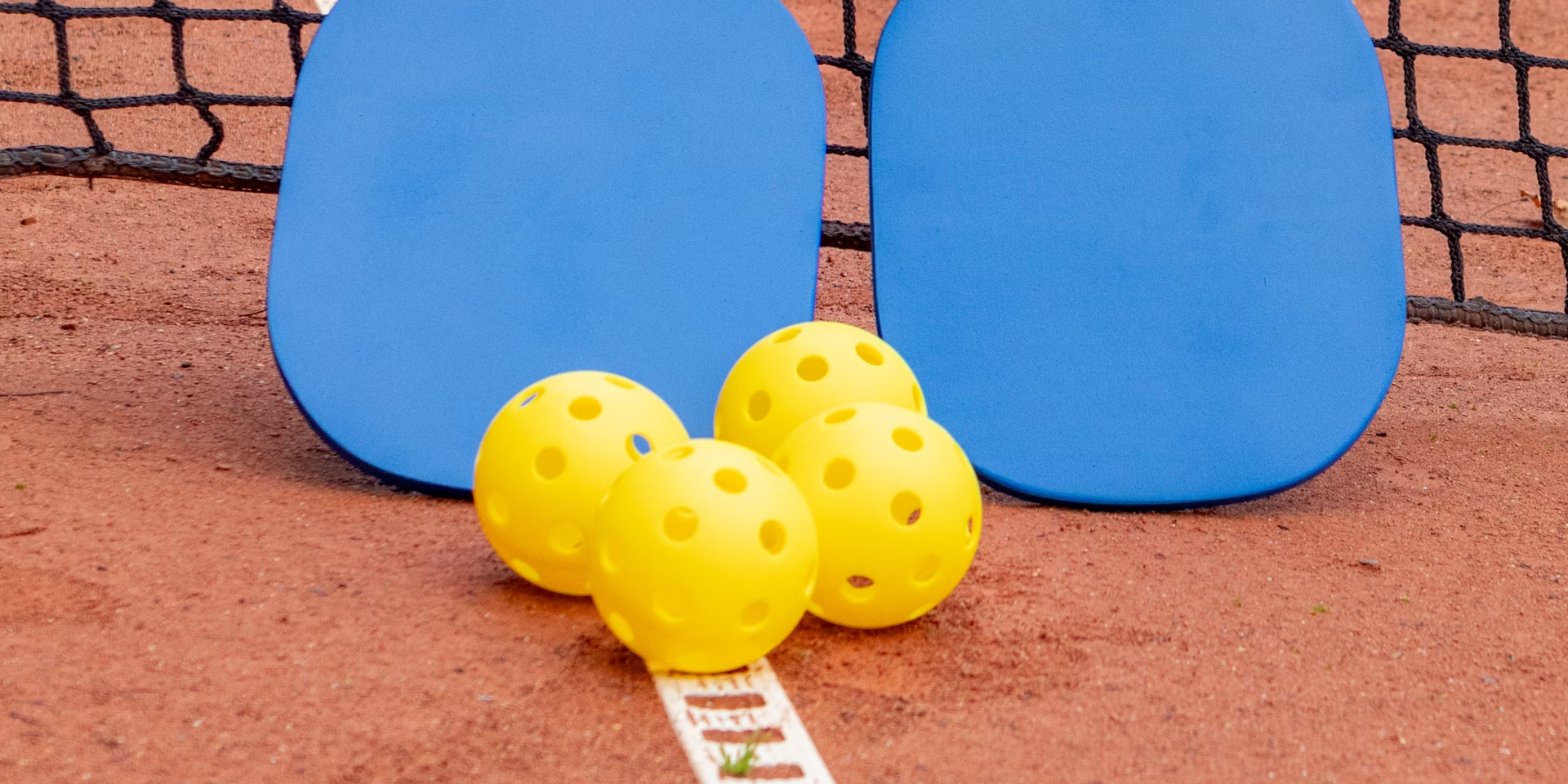 Four pickleballs sat in front of two pickleball paddles