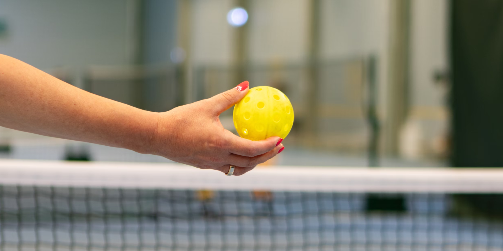 A pickleball players hand holding a pickleball