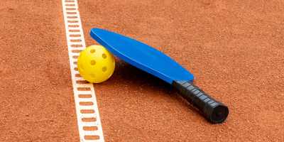 A pickleball paddle and ball on a court